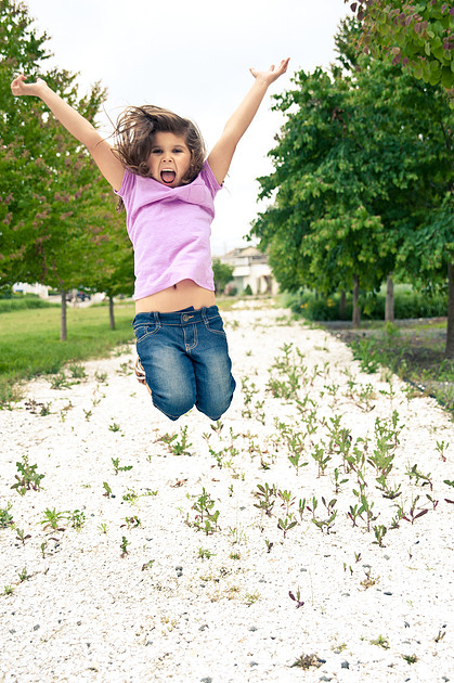 Young girl jumping joyfully outdoors, arms raised